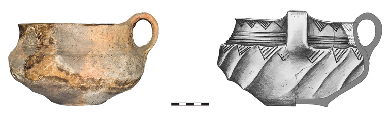 Kubek typu K22a, zdobiony pod krawędzią rytymi trójkątami zaszrafowanymi ukośnymi liniami, na szyjce – czterema poziomymi liniami rytymi, na brzuścu – ukośnymi, łukowatymi listewkami, na których znajdują się – przylegające do linii poziomych linii rytych – ryte trójkąty. Krawędź skośnie ścięta na zewnątrz, dno wyodrębnione. H – 11,5  cm (bez ucha), 13 cm (z uchem), R1 – 16,7  cm, R2 – 16,4 cm, R3 – 20,6  cm, R4 – 8,3  cm.